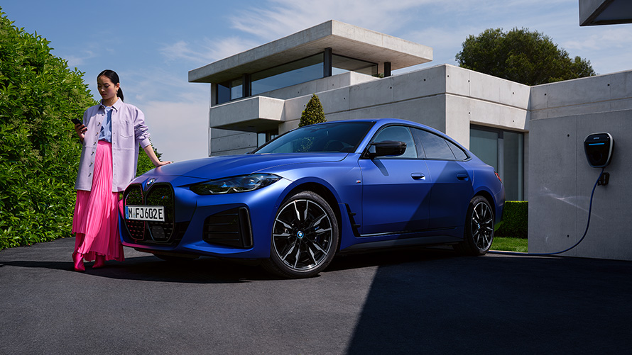 BMW i4 M50 G26 2021 BMW Individual Frozen Portimao Blue metallic three-quarter front view standing with woman in front of house