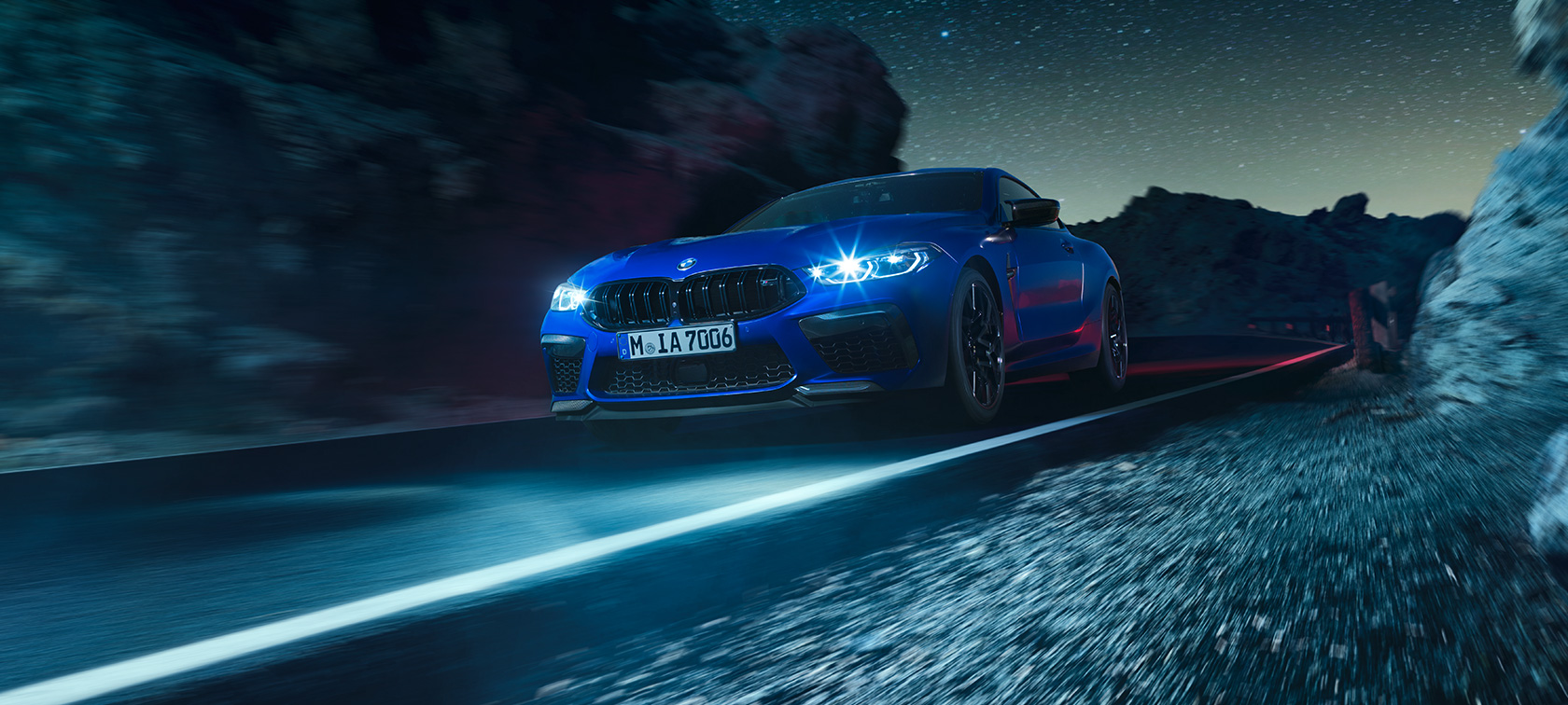 The BMW M8 Competition Coupé in Marina Bay Blue metallic, three-quarter front view, driving at night.