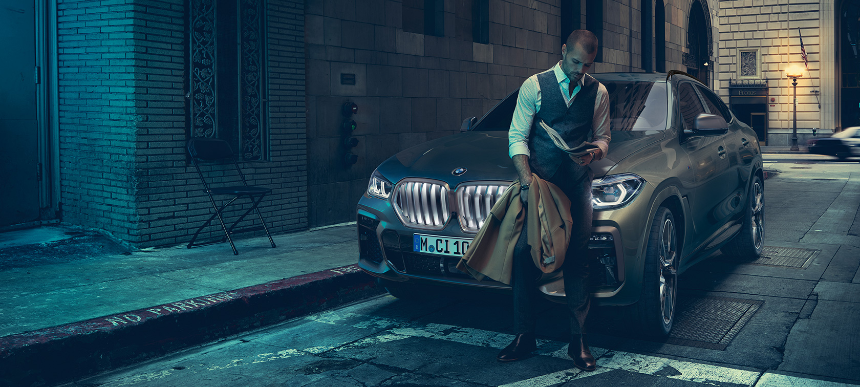 Man leaning on BMW X6 in lateral perspective in front of an urban setting.